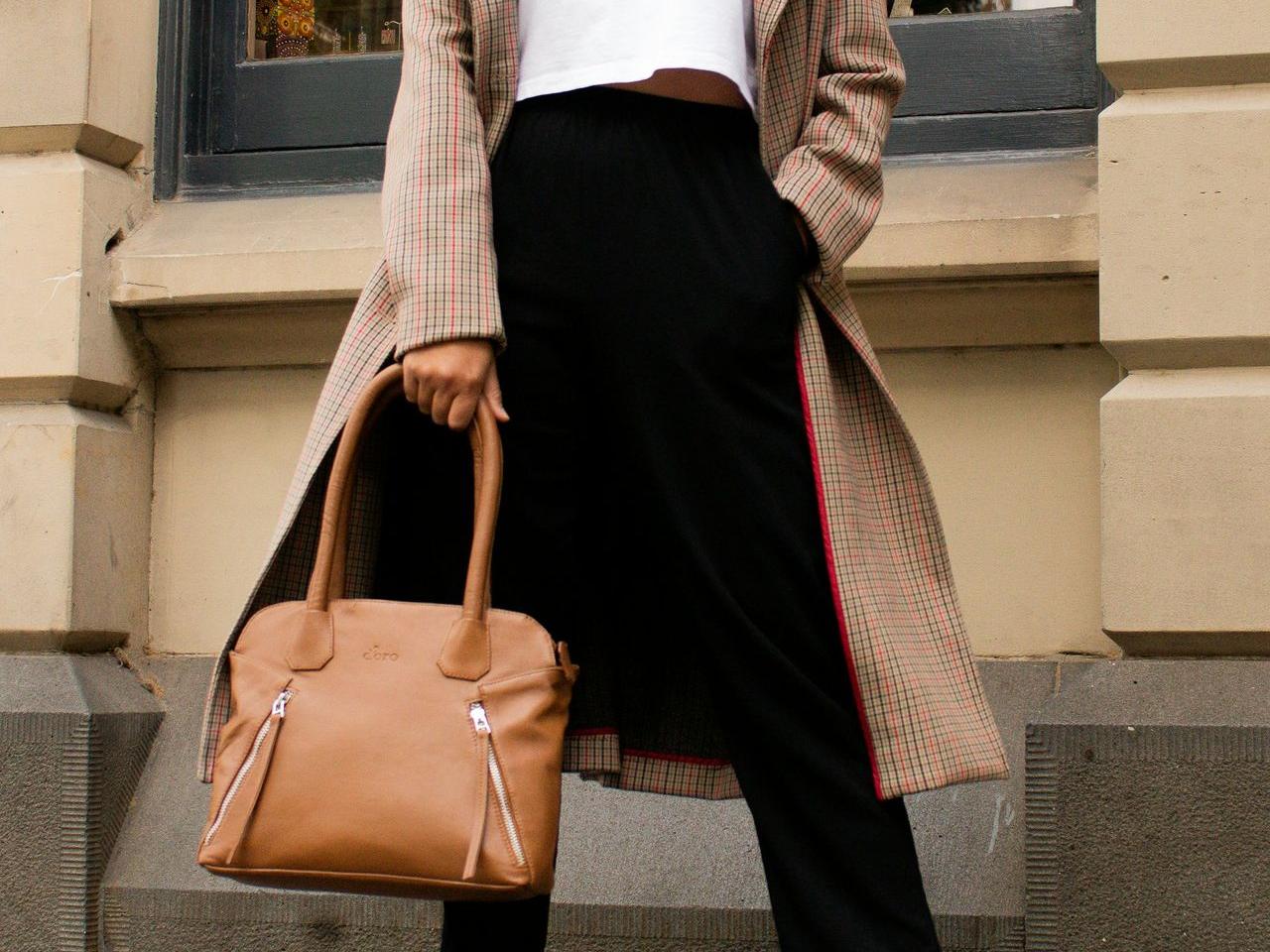 woman in white long sleeve shirt and black skirt holding brown leather handbag