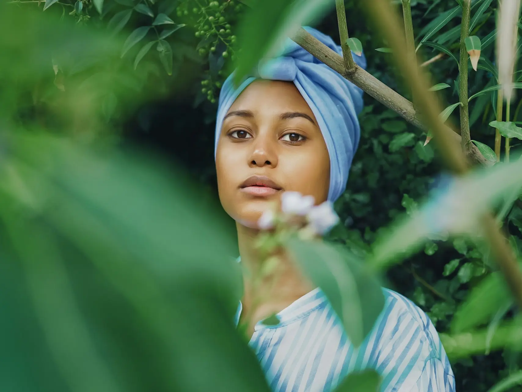 a woman wearing a blue turban standing in front of a bush