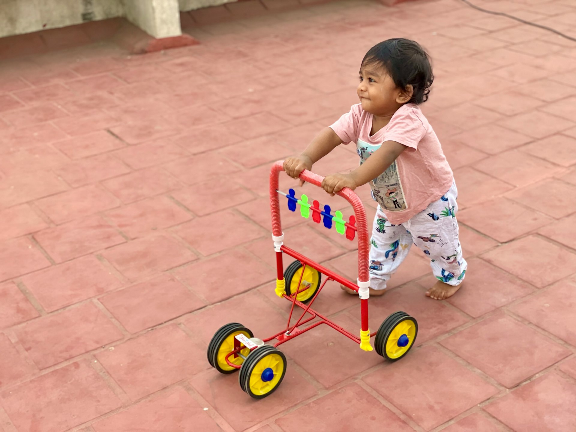 girl in white and pink floral dress riding red and yellow trike